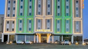 Ein mehrgeschossiges Hotel mit einer symmetrischen Fassade, gekennzeichnet durch beleuchtete, grüne Neonumrandungen um die Fenster und einen zentralen Eingang mit einem Schild.