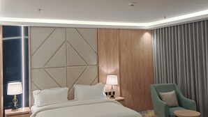 Ein modernes Hotelzimmer mit einem großen Bett, einem Nachttisch mit Lampe, einem grünen Sessel und einem gemusterten Boden.