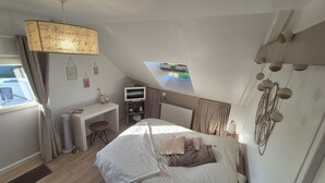 A bedroom with a bed, a desk, a chair, a TV, and a window with curtains.