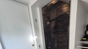 A modern bathroom with a shower, a white door, and a black mat.