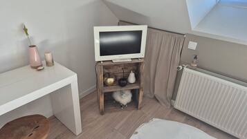 Une chambre moderne avec un plafond en pente, un bureau blanc, une chaise en bois, un téléviseur posé sur un meuble en bois et un radiateur.