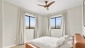 Une chambre à coucher avec un lit, un ventilateur de plafond et de grandes fenêtres avec des rideaux.