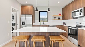 Une cuisine moderne dotée d’un îlot central, de meubles en bois, d’appareils électroménagers en acier inoxydable et offrant une vue sur l’extérieur.
