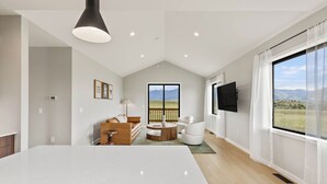 Un salon spacieux avec une grande table blanche, un canapé, une table basse ronde et un téléviseur fixé au mur.