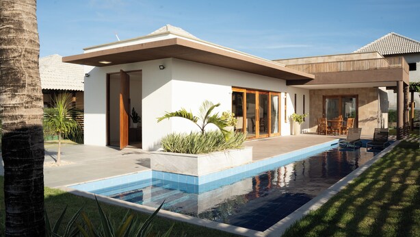 Una casa moderna amb piscina, un patió amb mobles d'exterior i un jardí amb palmeres.