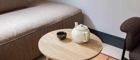 Una mesa de madera redonda con una tetera blanca y un bol oscuro sobre un sofá color beige.