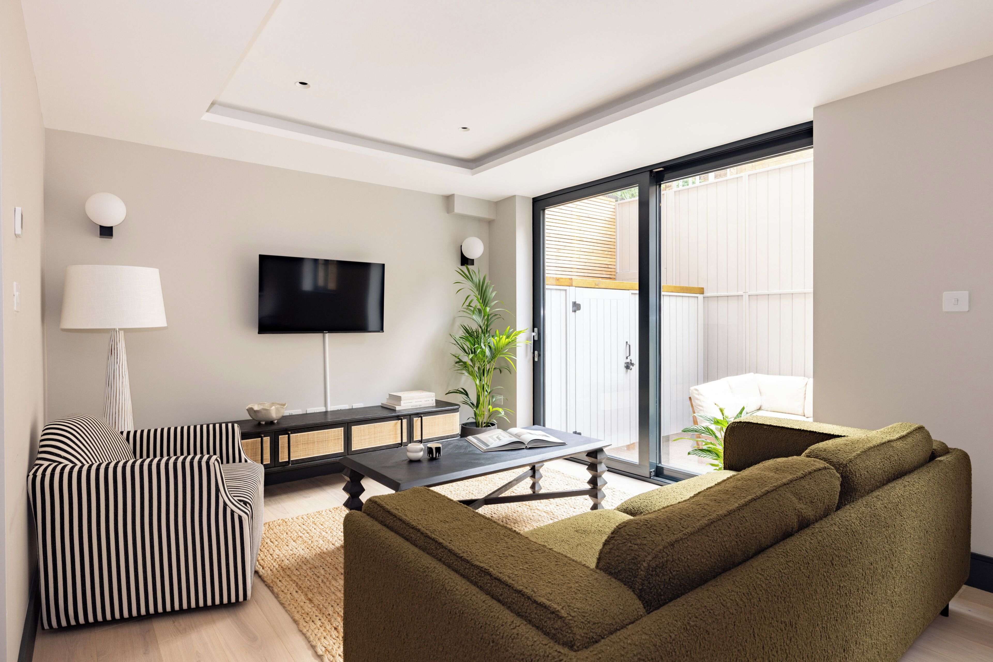 Una sala de estar moderna con un sofá, una mesa de centro, un televisor y un gran ventanal corredizo que da a un balcón.