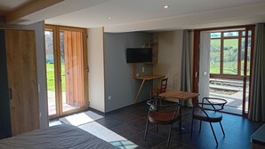 Un dormitorio con cama, escritorio con silla, televisor y vistas al exterior.
