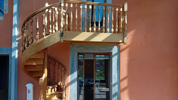 Una escalera de caracol de madera con un balcón, que conduce a una puerta de vidrio.