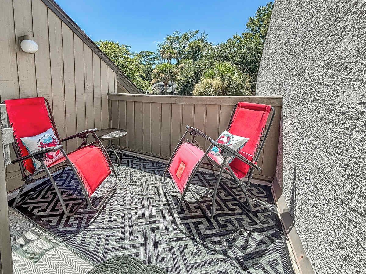 A patio with two red chairs and a small table, surrounded by a patterned rug.