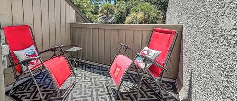A patio with two red chairs and a small table, surrounded by a patterned rug.