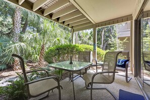 Une terrasse couverte avec une table en verre et des chaises en métal, entourée d’une végétation luxuriante.