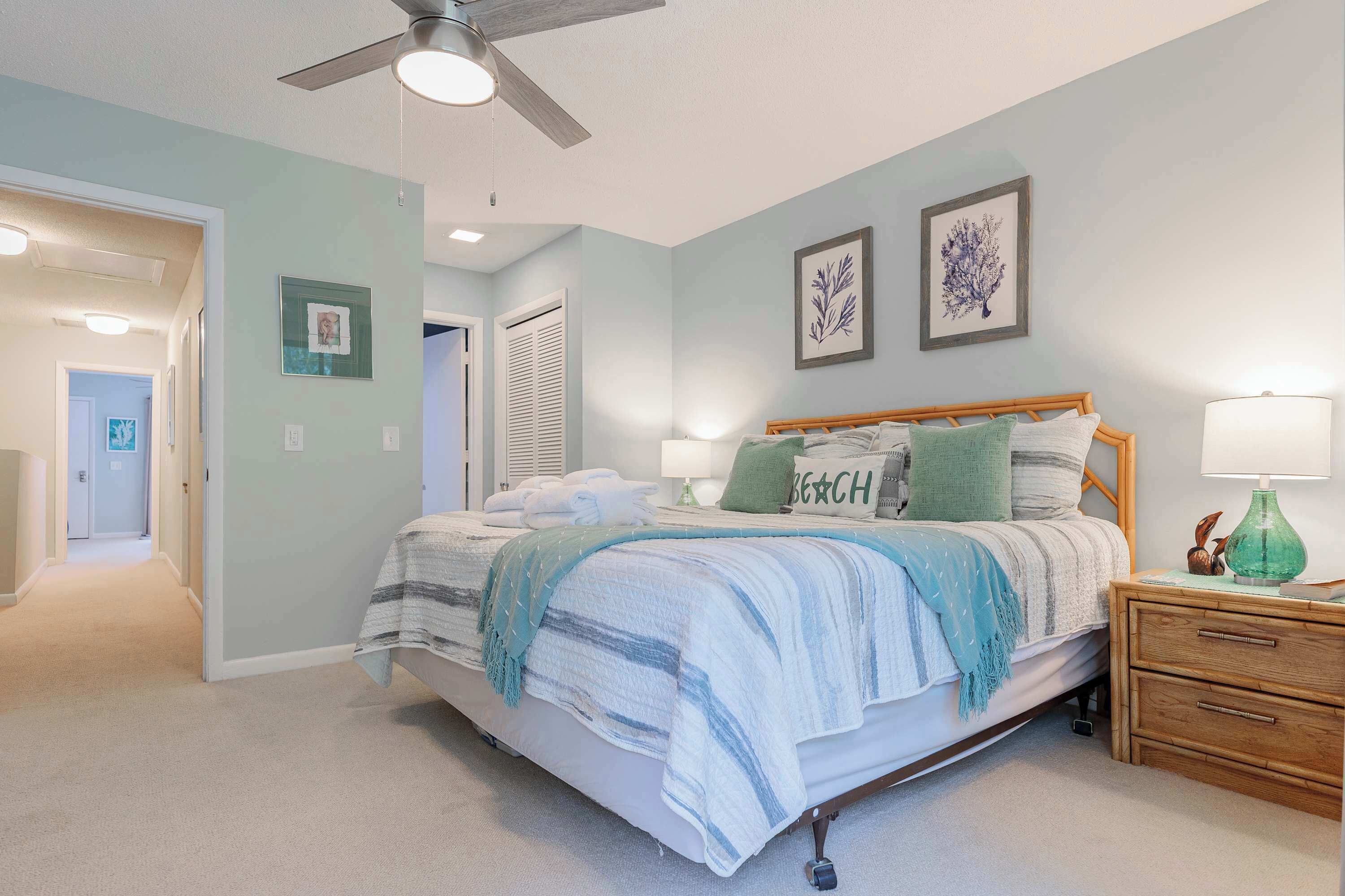 A bedroom with a bed, bedside tables, a ceiling fan, and wall art.