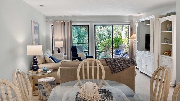Ein Wohnzimmer mit Glastisch, einer Couch, einem Fernsehschrank und Blick auf Grünflächen.