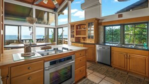 A modern kitchen with large windows, a built-in oven, and a dishwasher. - Kukuiula Bay House By Parrish - Oceanfront Family Home (Koloa)