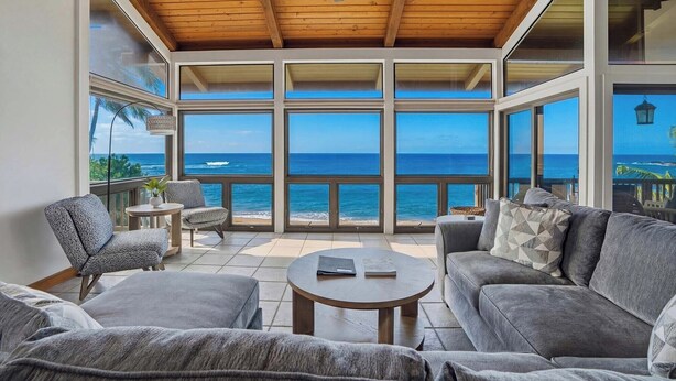 A spacious balcony with a view of the ocean, furnished with a sofa, chairs, and a small table. - Kukuiula Bay House By Parrish - Oceanfront Family Home (Koloa)