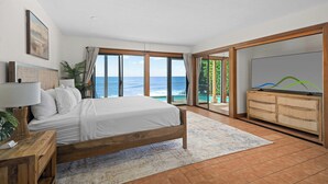 A bedroom with a bed, a TV, a wooden cabinet, and a view of the ocean. - Kukuiula Bay House By Parrish - Oceanfront Family Home (Koloa)
