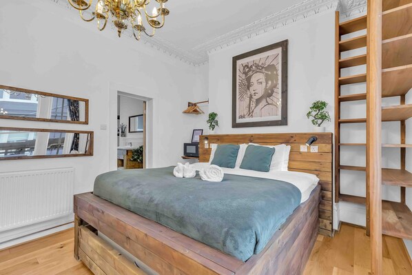 Une chambre à coucher avec un lit en bois, un grand miroir, un lustre et une œuvre d’art encadrée accrochée au mur.