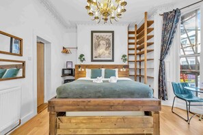 Une chambre avec un lit en bois, un lustre, un tableau encadré, une échelle en bois et une vue sur l’extérieur.