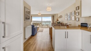 Une cuisine moderne avec des meubles blancs, un plan de travail en bois et une vue sur la mer grâce à de grandes fenêtres.