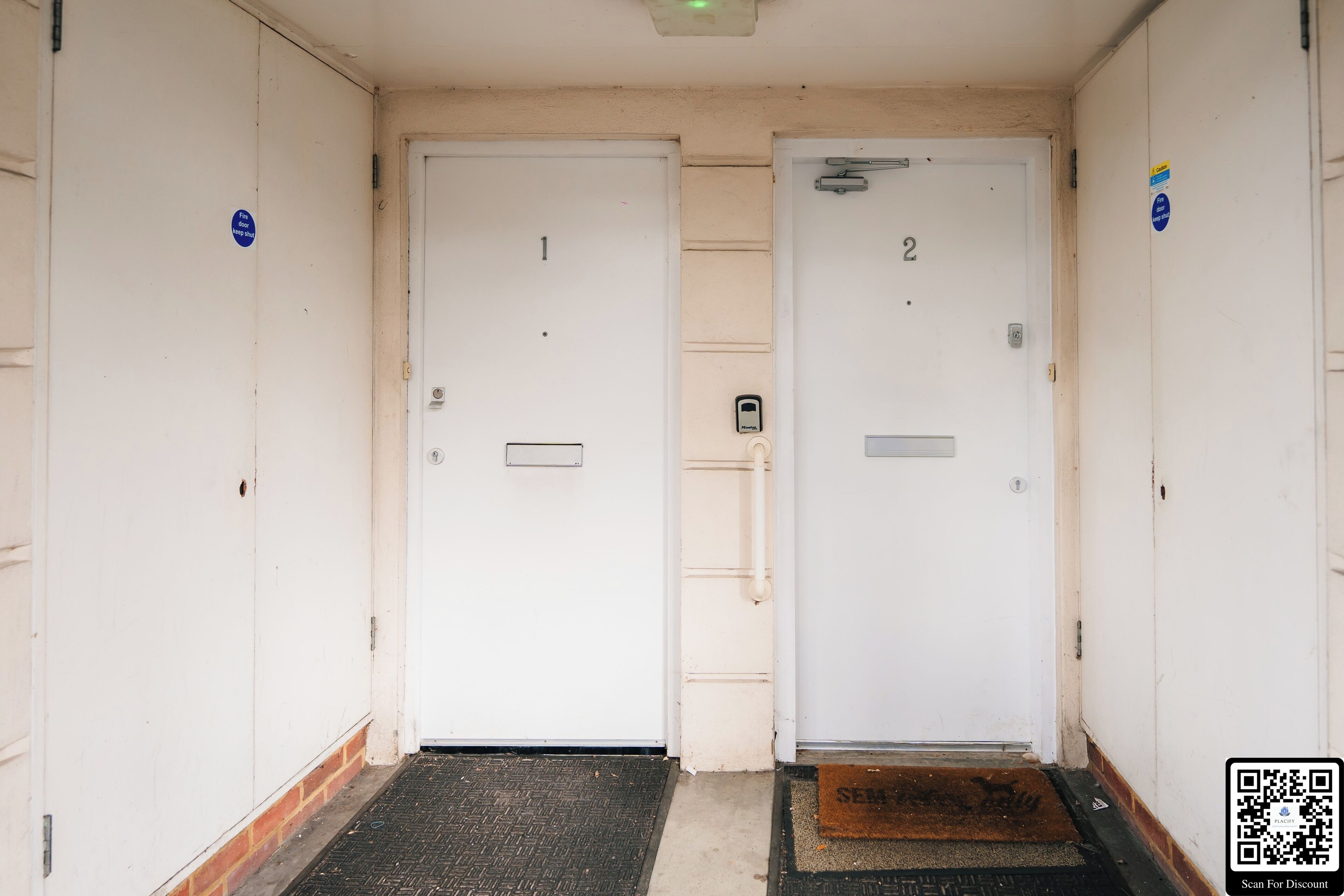 Un couloir avec deux portes, numérotées 1 et 2, et un paillasson à l’entrée.