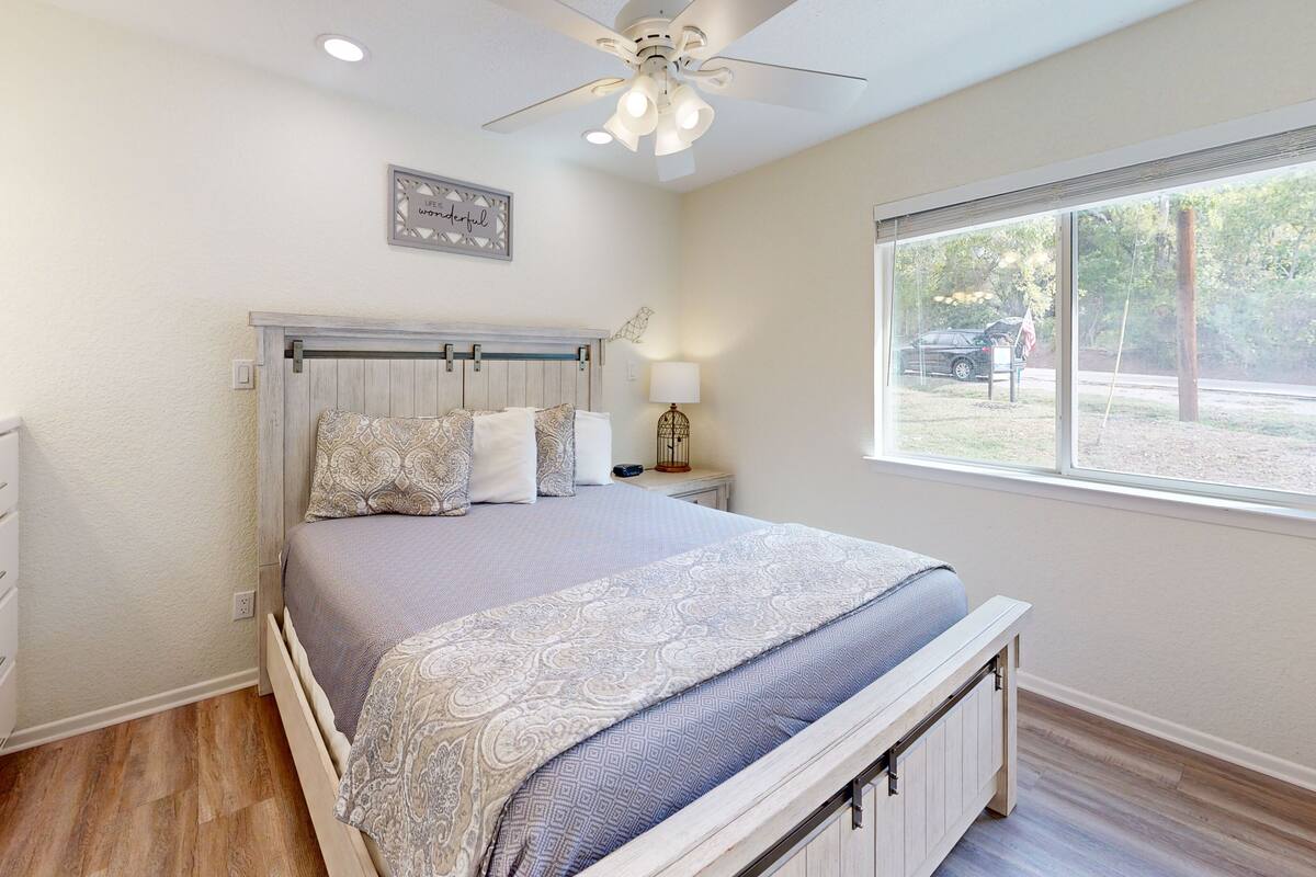 Un dormitorio con cama, mesita de noche, ventana y ventilador de techo.