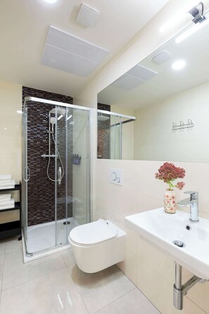 A modern bathroom with a glass-enclosed shower, a white toilet, and a sink with a vase of flowers.