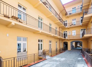 A multi-story residential building with balconies, a central courtyard, and a cobblestone ground.