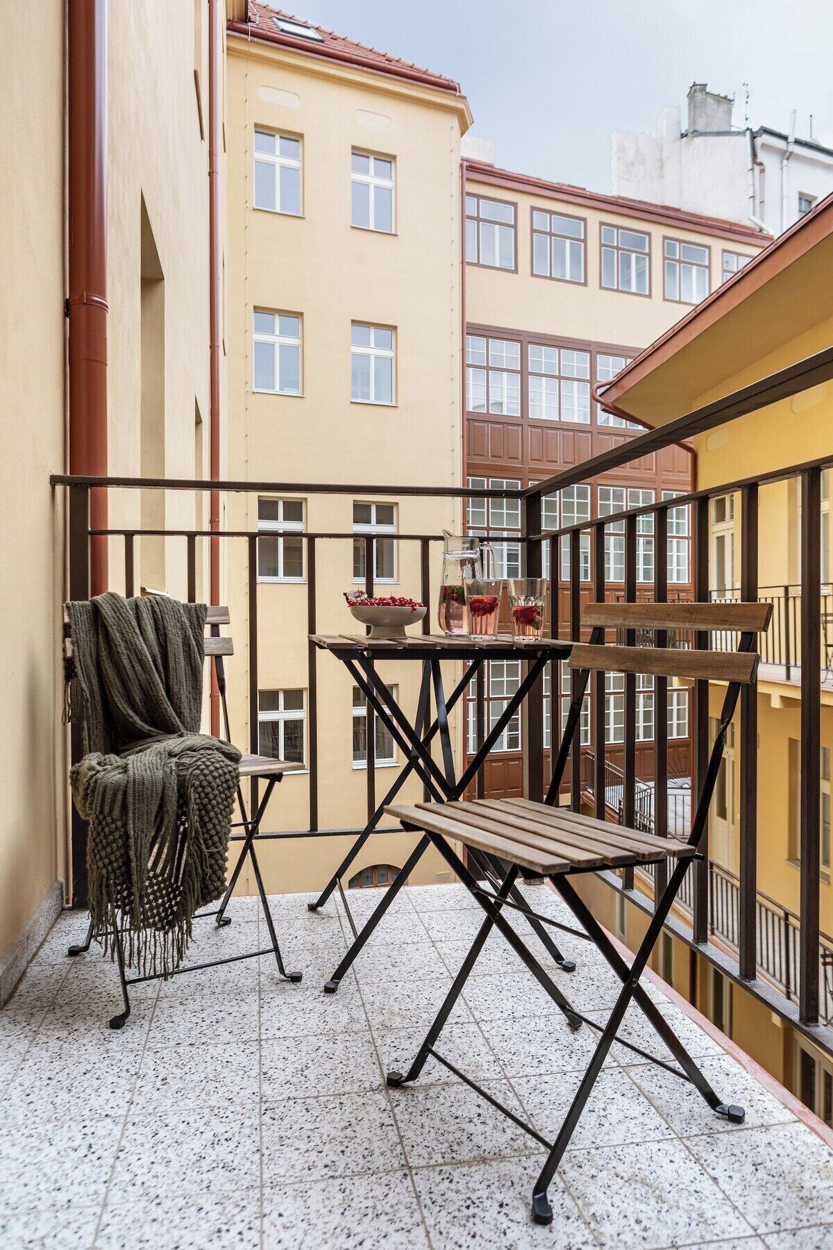 A balcony with a table and chairs, a chair with a blanket, and a bottle of water.