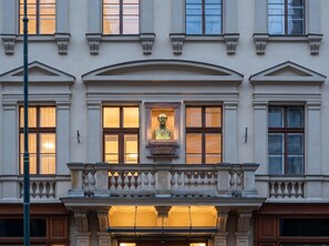 Eine Gebäudefassade mit einer zentralen Statue, mehreren Fenstern und einem Balkon mit Brüstungen.