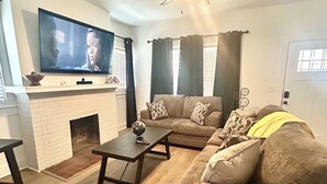 Uma sala de estar com lareira, sofá, mesa de centro e televisão na parede.