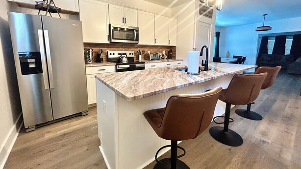 Cozinha moderna com ilha central, eletrodomésticos de aço inoxidável e área de refeições com banquetas.