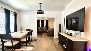 Uma sala de estar moderna com área de jantar, televisão de tela plana e uma janela grande com cortinas.