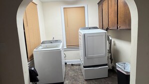 A laundry room with a washing machine, dryer, and a trash bin. - The Sunny Cottage minutes to downtown (Florence)