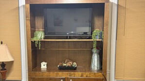 A wooden cabinet with a flat-screen TV, decorative plants, and a small house model. - The Sunny Cottage minutes to downtown (Florence)