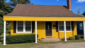 A yellow single-story house with a brown roof, white window frames, and a brick chimney. - The Sunny Cottage minutes to downtown (Florence)