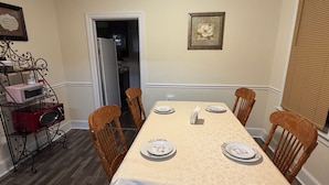 A dining room with a table set for four, surrounded by wooden chairs, a microwave on a metal rack, and framed artwork on the walls. - The Sunny Cottage minutes to downtown (Florence)