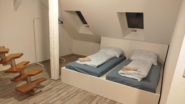 A small, modern room with a loft-style bed, a wooden staircase, and a small window. - AriProp Chemnitz Central Stay – 3 Guests (Chemnitz)