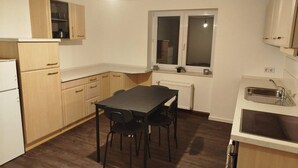 A compact kitchen with wooden cabinets, a dining table with chairs, a window, and a built-in sink. - AriProp Chemnitz Central Stay – 3 Guests (Chemnitz)