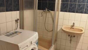 A compact bathroom with a washing machine, a shower enclosure, and a sink. - AriProp Chemnitz Central Stay – 3 Guests (Chemnitz)