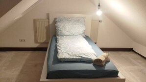 A small, single-bed room with a sloped ceiling, a radiator, and a bedside lamp. - AriProp Chemnitz Central Stay – 3 Guests (Chemnitz)