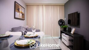 Et moderne spiseområde med et glasbord dækket til to personer, en sofa, et fjernsyn og en ventilator.