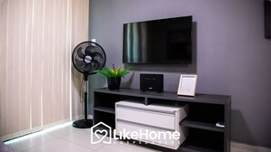 En moderne stue med et fladskærms-tv på væggen, en gulvventilator, en lille potteplante og et hvidt opbevaringsskab.