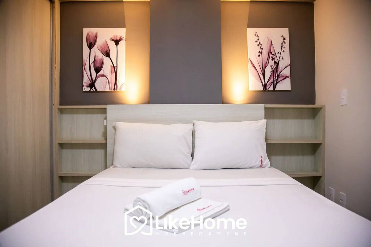 A hotel room with a bed, two pillows, a folded towel, and two wall-mounted artworks depicting flowers.