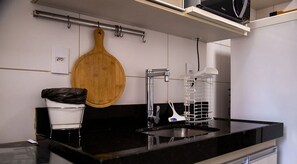 A modern kitchen with a black countertop, stainless steel sink, and a wooden cutting board hanging on the wall. - Antonino Cavalcanti - LikeHome Accommodations (João Pessoa)