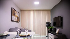 A modern dining area with a glass table set for two, a sofa, a TV, and a fan. - Antonino Cavalcanti - LikeHome Accommodations (João Pessoa)