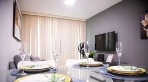 Ein moderner Essbereich mit einem Glastisch, gedeckt für vier Personen, mit gemusterten Tellern und klaren Gläsern.