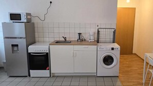 Une cuisine compacte équipée d’un four à micro-ondes, d’un réfrigérateur, d’un four, d’un évier, d’une machine à café et d’un lave-linge.