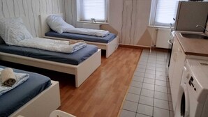 Une chambre d’hôtel compacte avec deux lits simples, une petite kitchenette et un lave-linge.
