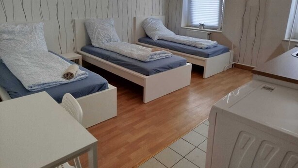Une petite chambre moderne avec deux lits simples, un bureau blanc et une fenêtre équipée de stores.